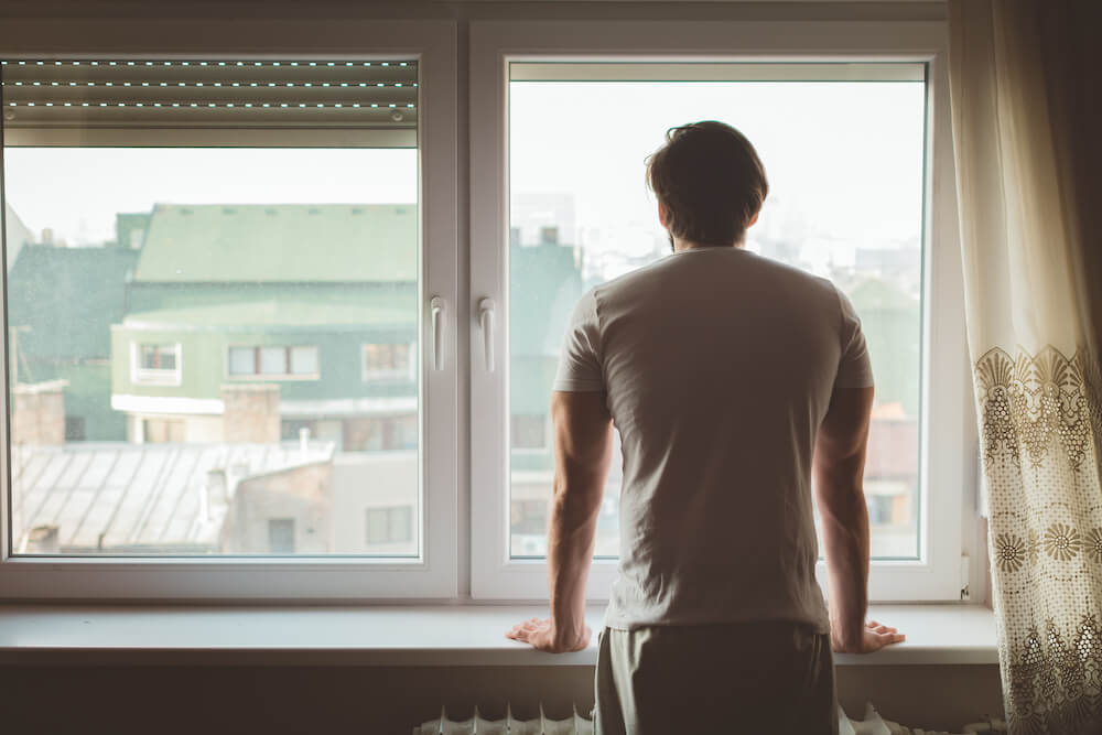 Foto de homem de costas em frente a uma janela olhando para fora